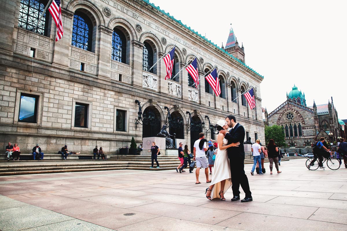 A bride and groom share a kiss in front of the Boston Public Library