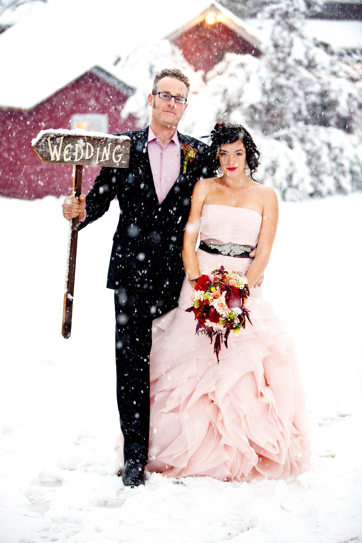 the bride and groom holding a wedding sign in the snow at Race Brook Lodge