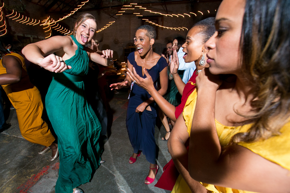 Guests are caught up in a vibrant dance at a wedding reception, expressing their joy and energy. A sea of colors from their festive attire adds to the lively atmosphere.